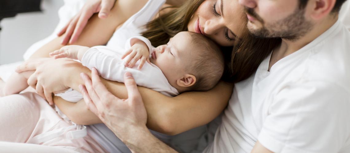 Mãe sendo abraçada pelo parceiro enquanto carrega bebê no colo