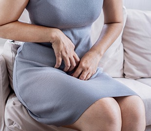 Mulher sentada com as mãos na região pélvica, expressando desconforto ou coceira, simbolizando sintomas de candidíase ou vaginose bacteriana.
