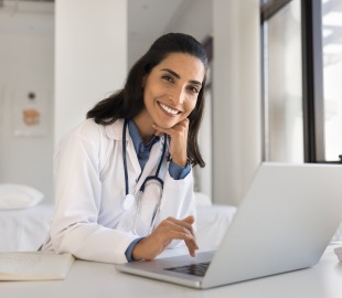 Médica sorridente em consultório realiza atendimento online por telemedicina, representando especialidades médicas com consultas virtuais