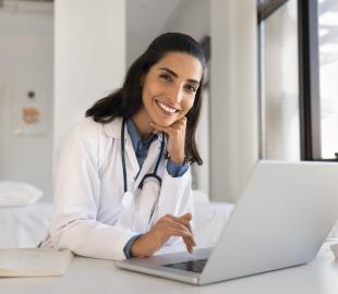 Médica sorridente em consultório realiza atendimento online por telemedicina, representando especialidades médicas com consultas virtuais