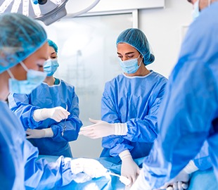 Equipe cirúrgica vestindo aventais e máscaras em uma sala de cirurgia, com foco em uma paciente sob o pano cirúrgico, simbolizando procedimentos médicos de emergência e cirurgias.
