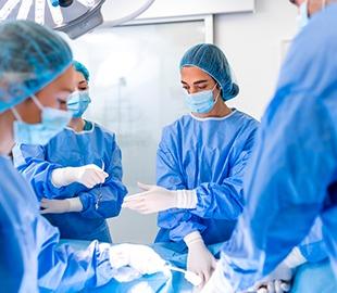 Equipe cirúrgica vestindo aventais e máscaras em uma sala de cirurgia, com foco em uma paciente sob o pano cirúrgico, simbolizando procedimentos médicos de emergência e cirurgias.