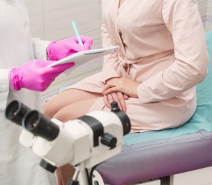 Consulta ginecológica onde uma médica de luvas rosas anota informações em uma prancheta, enquanto uma paciente senta na maca. Em primeiro plano, um colposcópio, simbolizando exames ginecológicos e saúde da mulher.