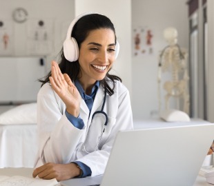 Médica sorridente com fones de ouvido realiza consulta online por videoconferência, simbolizando o funcionamento da telemedicina e o atendimento médico à distância.