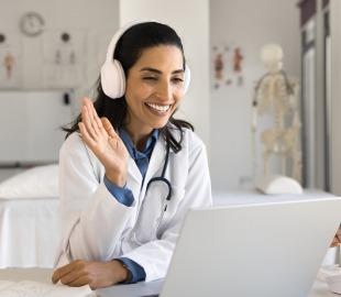 Médica sorridente com fones de ouvido realiza consulta online por videoconferência, simbolizando o funcionamento da telemedicina e o atendimento médico à distância.