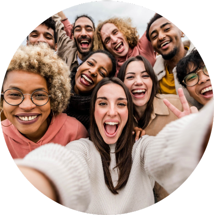 Grupo de nove pessoas sorridentes reunidas para uma selfie, com foco no rosto de quem segura a câmera ao centro. Todos estão próximos, em clima de descontração e amizade, com fundo desfocado que destaca os rostos e expressões.