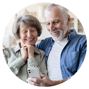 Casal de idosos sorrindo enquanto conversa por videochamada no celular.