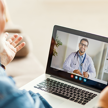 Médico sorrindo e gesticulando durante uma teleconsulta em um notebook.