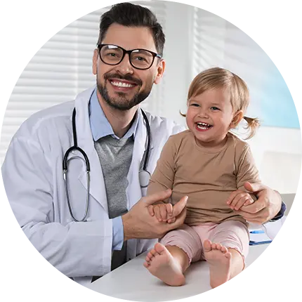 Profissional de saúde com jaleco branco, óculos e estetoscópio no pescoço segura criança sorridente sentada sobre mesa de exame, com pés descalços visíveis. Cena ocorre em consultório médico com persianas ao fundo, representando atendimento pediátrico humanizado.