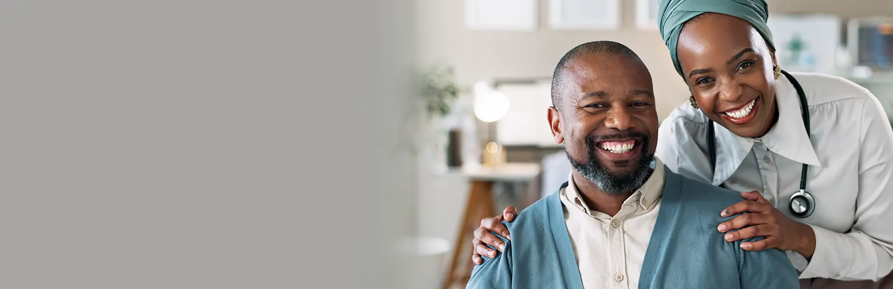 Duas pessoas interagindo; o homem está sentado e sorrindo, enquanto a mulher parece oferecer cuidado ou apoio, em ambiente interno.