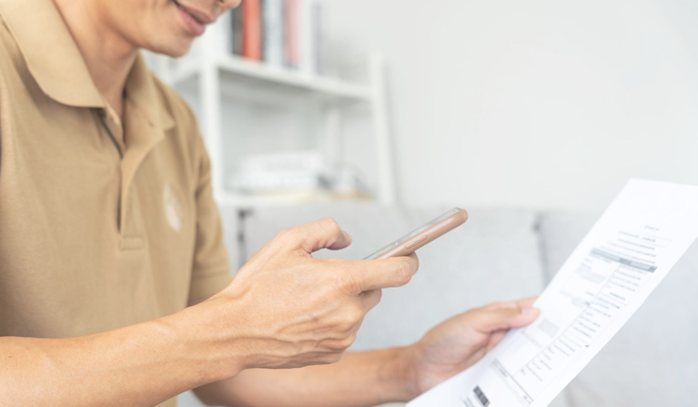 Foco de uma mão com o smartphone e um exame na frente.
